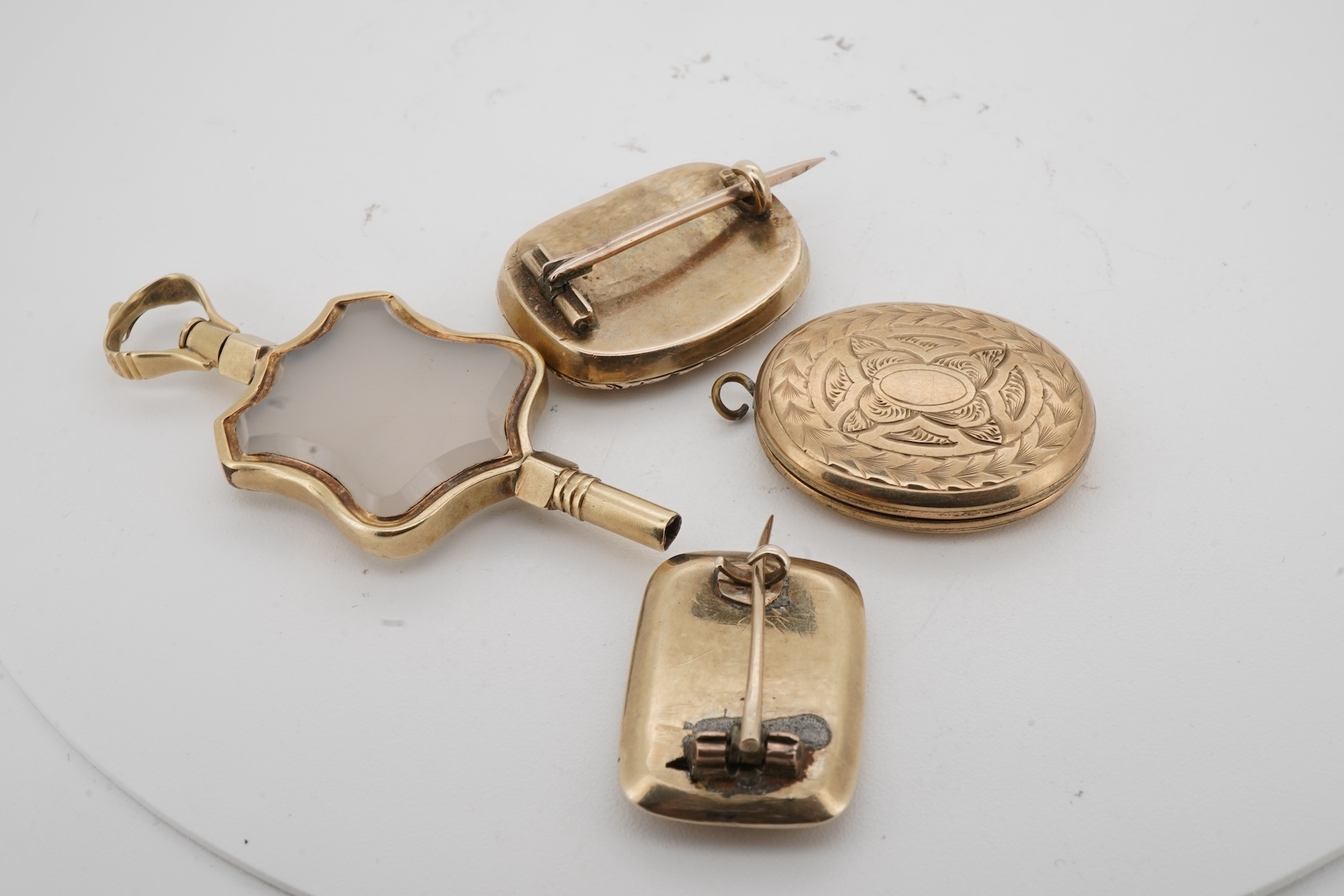 A locket, a watch key and two mourning brooches, the oval locket engraved with foliate details, opening to reveal a glazed panel of hairwork; together with two early 19th century mourning brooches, engraved with flowers